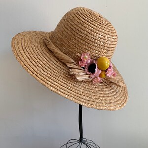 Pu&ograve; includere: Un cappello di paglia a tesa larga con un'abbellimento floreale giallo e rosa. Il cappello &egrave; fatto di paglia intrecciata e ha una tesa larga e morbida. I fiori sono di tessuto e sono attaccati al cappello con un piccolo nastro.