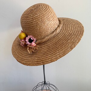 Pu&ograve; includere: Un cappello di paglia per il sole con un'ampia tesa e un nastro marrone. Il cappello &egrave; decorato con fiori rosa e limoni gialli.