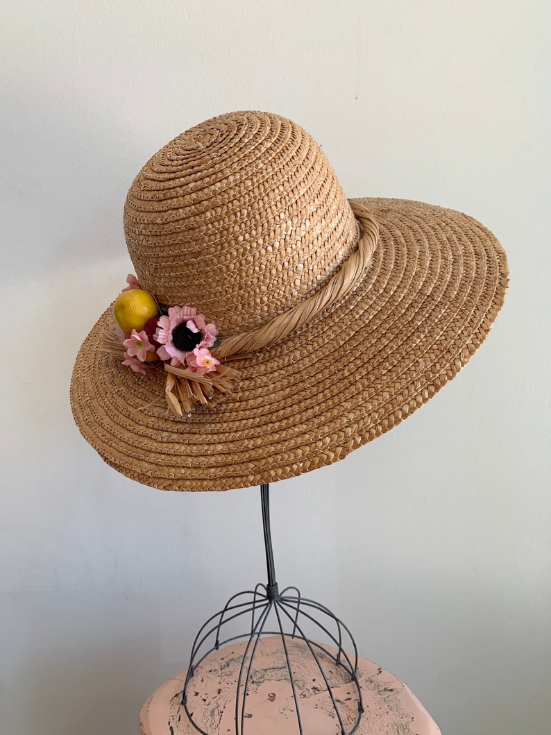 Pu&ograve; includere: Un cappello di paglia per il sole con un'ampia tesa e un nastro marrone. Il cappello &egrave; decorato con fiori rosa e limoni gialli.