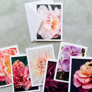 May include: A collection of rectangular greeting cards featuring high-resolution floral photography. The cards display various blossoms including a pale pink peony, a vibrant coral flower, a white dahlia, a deep purple bloom, and a purple orchid.