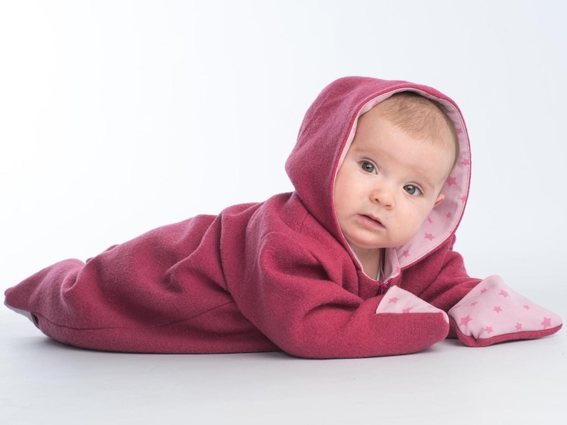 Baby trägt einen warmen SOLE Kapuzenstrampler mit Reißverschluss und langen Ärmeln, Vorderansicht des fertigen Baby Overalls.