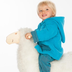 May include: A bright turquoise hooded fleece jacket with dark blue striped cuffs and a matching pocket, worn over dark blue and turquoise striped trousers, while sitting on a white plush toy sheep with a smooth wooden head and handle.