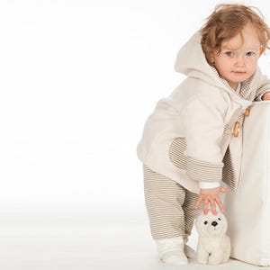 Kind lehnt an Würfel, komplett Outfit sichtbar, creme Kapuzenjacke mit Holzverschlüssen, pdf schnittmuster babykleidung