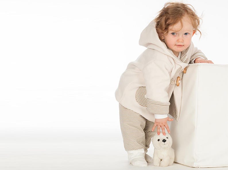 Kind lehnt an Würfel, komplett Outfit sichtbar, creme Kapuzenjacke mit Holzverschlüssen, pdf schnittmuster babykleidung