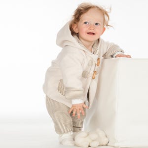Kind steht halb hinter Würfel, creme Walkjacke mit Streifenfutter, betont kuschelige babyjacke schnittmuster