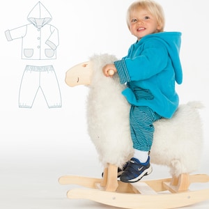 May include: A young child wearing a blue hooded jacket and striped pants rides a white rocking horse. The child is smiling and looking to the left. A pattern for a hooded jacket and pants is shown in the background.
