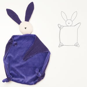 May include: A plush security blanket featuring a purple velvet square body with knotted corners and a rabbit head. The rabbit has long ears with a purple and white polka dot pattern, a cream-colored face, and a black embroidered nose. A line drawing of the rabbit is shown to the right.
