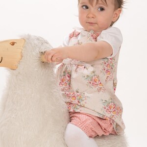 Baby sitzt auf Schaf, trägt geblümtes Trägerkleid, zeigt trägerkleid baby schnittmuster Look