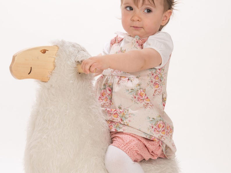 Baby sitzt auf Schaf, trägt geblümtes Trägerkleid, zeigt trägerkleid baby schnittmuster Look