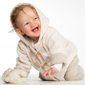 Nahaufnahme lachendes Kind am Boden, Kapuze auf, Holzverschlüsse sichtbar, cosy baby set schnittmuster pdf