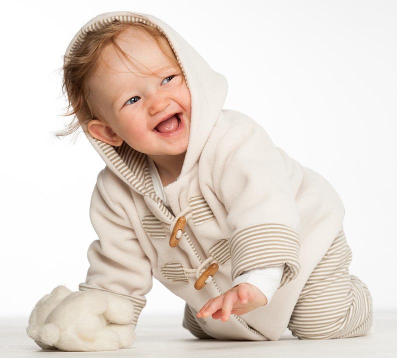 Nahaufnahme lachendes Kind am Boden, Kapuze auf, Holzverschlüsse sichtbar, cosy baby set schnittmuster pdf