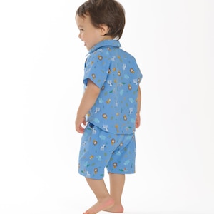 May include: A toddler wearing a blue short-sleeved shirt and matching shorts with a pattern of animals and plants. The shirt has a button-up collar.
