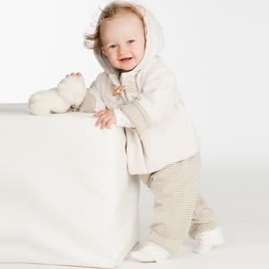 Seitliche Aufnahme, Kind lehnt lächelnd an Würfel, kuschelige Kapuzenjacke, babyjacke pdf schnittmuster