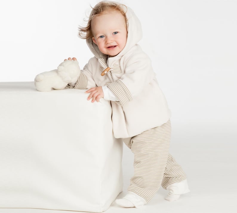 Seitliche Aufnahme, Kind lehnt lächelnd an Würfel, kuschelige Kapuzenjacke, babyjacke pdf schnittmuster