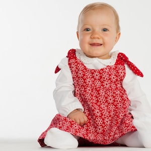 Sitzendes Baby im roten Schürzenkleid über Shirt, zeigt schürzenkleid schnittmuster Styling idee