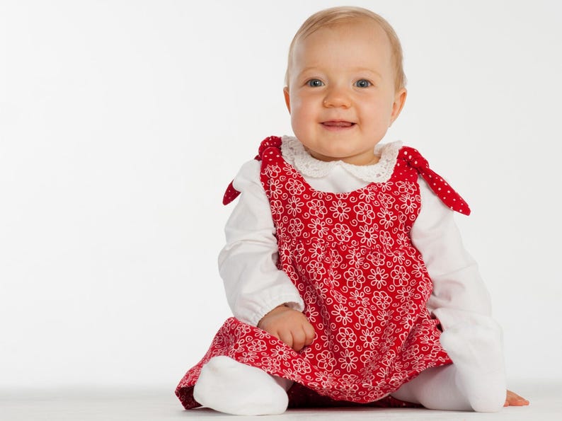 Sitzendes Baby im roten Schürzenkleid über Shirt, zeigt schürzenkleid schnittmuster Styling idee