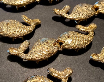 May include: A set of gold-toned metal fish-shaped decorative pieces. The fish are detailed with scales and have open mouths.