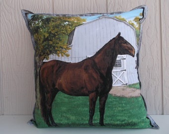 May include: A decorative pillow with a brown horse standing in a field in front of a white barn. The pillow has a blue and green background.