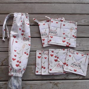 May include: Set of eight white cotton pot holders with red hearts and cherries. The pot holders have the text "Kiss the Baker" and "Bless the Baker" printed on them.