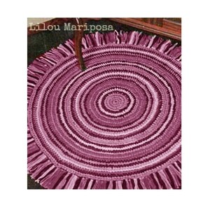 May include: A round, crocheted rug with a fringe border in shades of pink and purple. The rug has a concentric circle pattern.