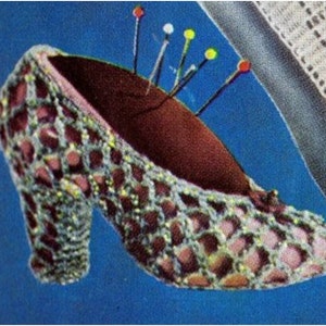 May include: A crocheted shoe with a brown fabric insole and multiple pins sticking out of it. The shoe is on a blue background.