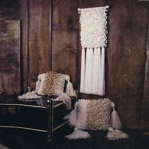May include: Three white and brown fluffy pillows with tassels. The pillows are on a black glass table with gold metal legs. A white wall hanging with tassels is on the wall behind the table.