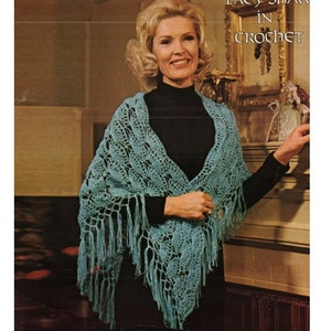 May include: A woman wearing a teal crochet shawl with fringe. The shawl has a lacy pattern and is draped over her shoulders. The text "Lacy Shaw in Crochet" is visible in the top right corner of the image.