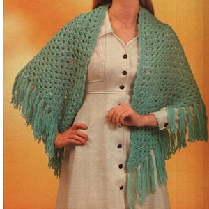 May include: A teal crochet shawl with fringe. The shawl is draped over a person wearing a white dress.
