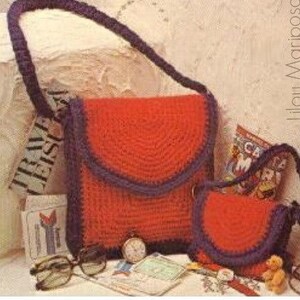 May include: Two crocheted bags, one red and one smaller red, with a purple trim. The bags have a rounded flap and a strap. The bags are sitting on a table with other items.