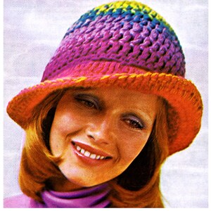 May include: A woman wearing a crocheted hat with a rainbow color gradient. The hat has a wide brim and is made with a textured stitch.