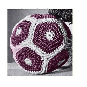 May include: A crocheted soccer ball with a purple and white color scheme. The ball is made of multiple crocheted panels that are joined together to form a sphere.