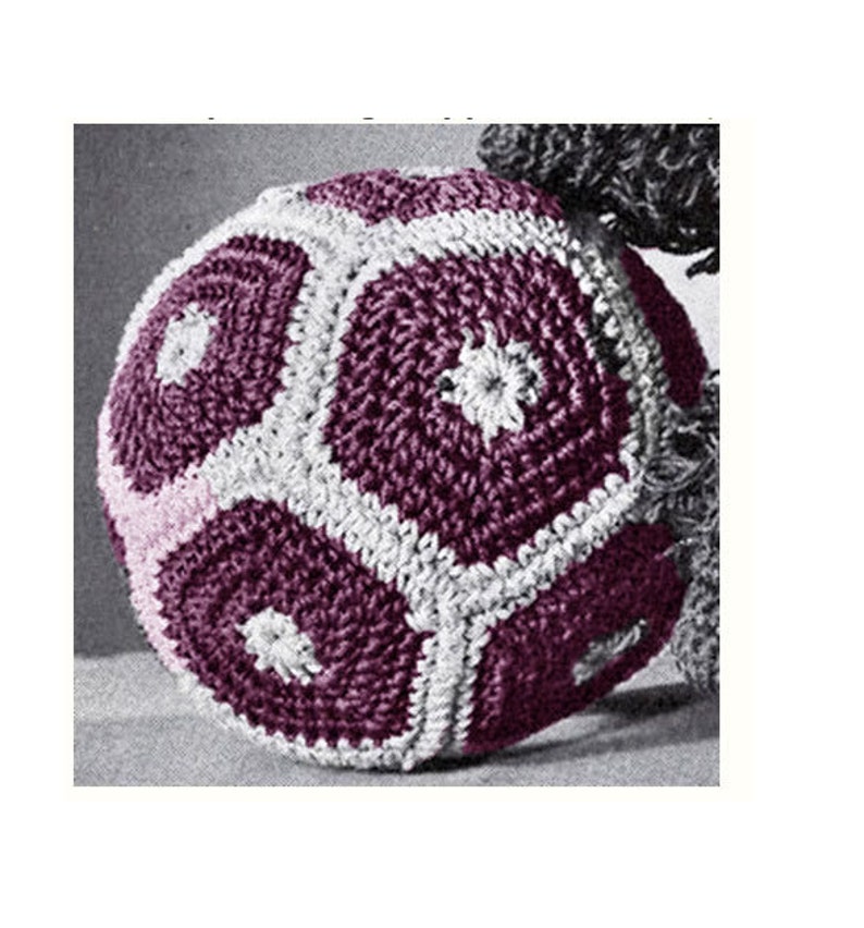 May include: A crocheted soccer ball with a purple and white color scheme. The ball is made of multiple crocheted panels that are joined together to form a sphere.