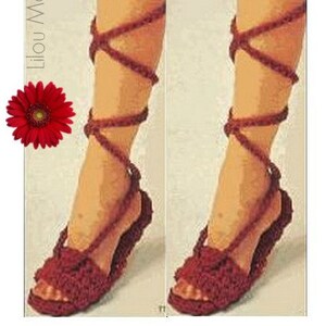 May include: A pair of handmade, burgundy crochet sandals with ankle straps. The sandals feature a woven design on the footbed and straps that wrap up the leg. A red gerbera daisy is in the upper left corner.