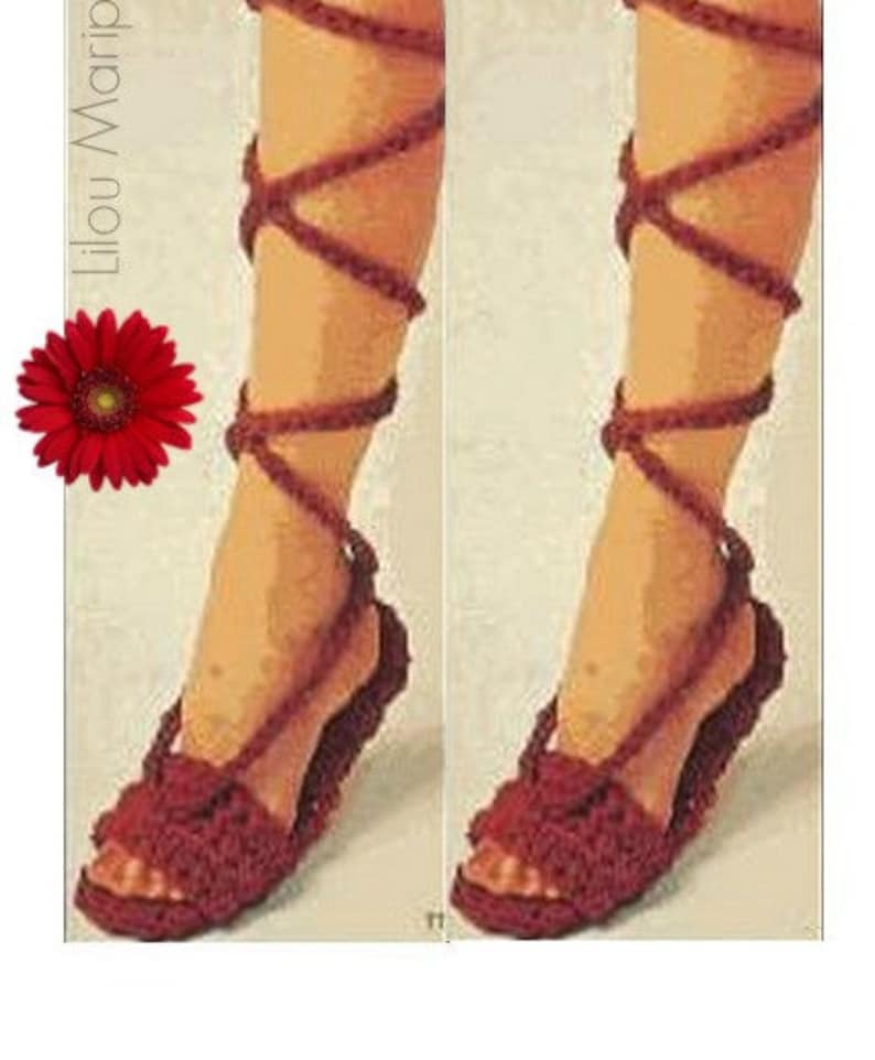 May include: A pair of handmade, burgundy crochet sandals with ankle straps. The sandals feature a woven design on the footbed and straps that wrap up the leg. A red gerbera daisy is in the upper left corner.