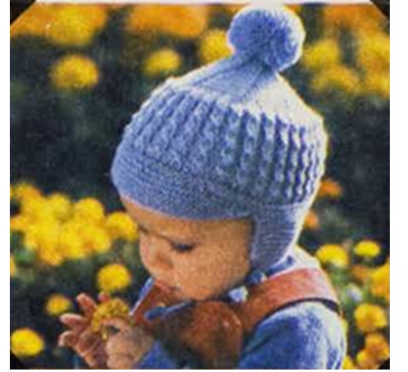 May include: A blue knitted baby hat with a pom-pom on top. The hat has a textured pattern and ear flaps.