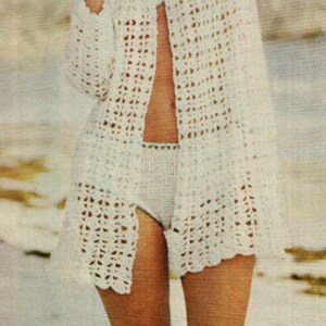 May include: A white crochet cardigan with a light blue tie at the neckline. The cardigan is open at the front, revealing a white crochet bikini bottom.