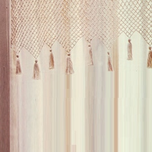 May include: A beige crocheted curtain with a fringe of tassels. The curtain is made of a delicate, open-weave fabric.