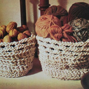 May include: Two crocheted baskets filled with yarn and nuts. The baskets are made of natural beige rope and have a woven pattern. The yarn is in shades of brown, pink, and gray. The nuts are brown and have a rough texture.