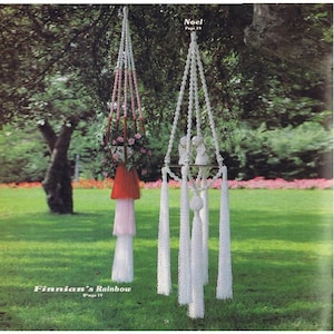 Puede incluir: Dos macramés para colgar plantas, uno blanco y otro con detalles en rosa y rojo, colgados de una rama de árbol. El macramé blanco tiene una pequeña bola blanca y borlas. El macramé rosa y rojo tiene una borla roja y una borla rosa. Ambos macramés están etiquetados con sus nombres y números de página.