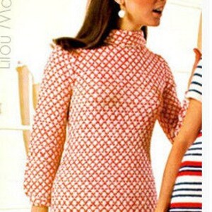 May include: A woman wearing a red and white geometric patterned dress with a high neck and long sleeves.