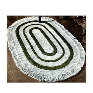 May include: Oval-shaped rug with a white and olive green design. The rug features an oval pattern with a fringe border. The text "Lilou Mariposa" is visible on the right side of the rug.