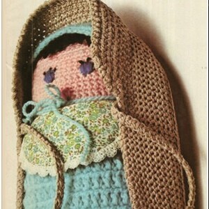 May include: A crocheted doll with a brown hooded coat, a pink face, blue eyes, and a blue and white floral dress.