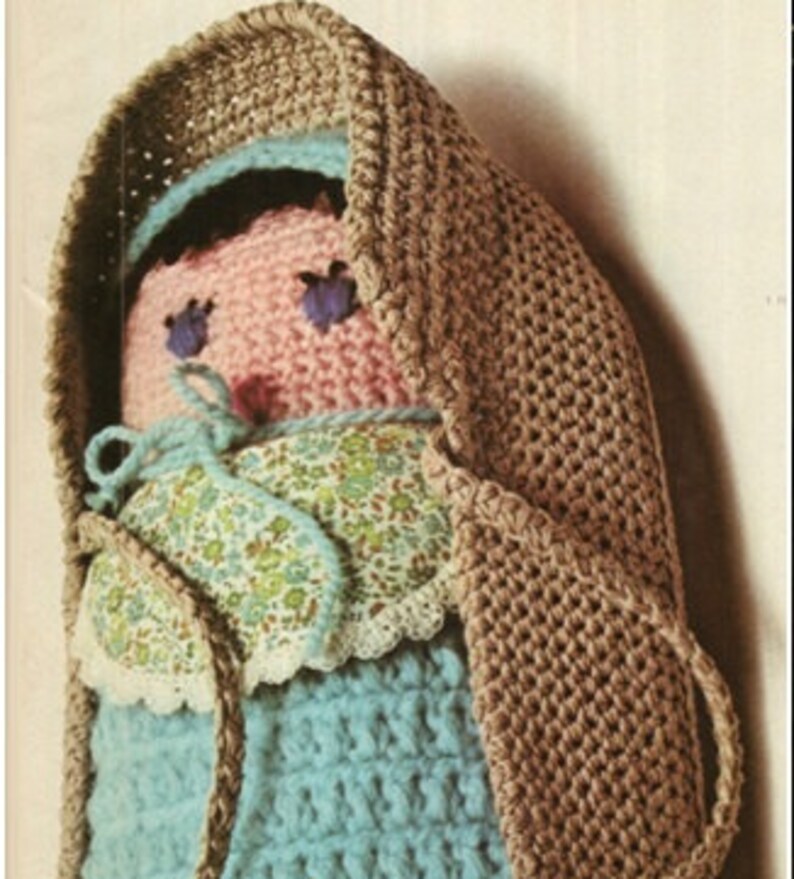 May include: A crocheted doll with a brown hooded coat, a pink face, blue eyes, and a blue and white floral dress.