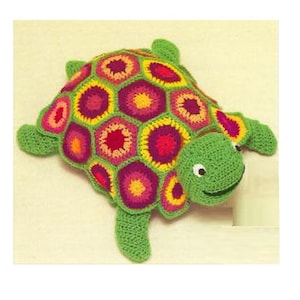 May include: A crocheted turtle toy with a green shell and a colorful, geometric pattern on its back. The turtle has a smiling face with black eyes.