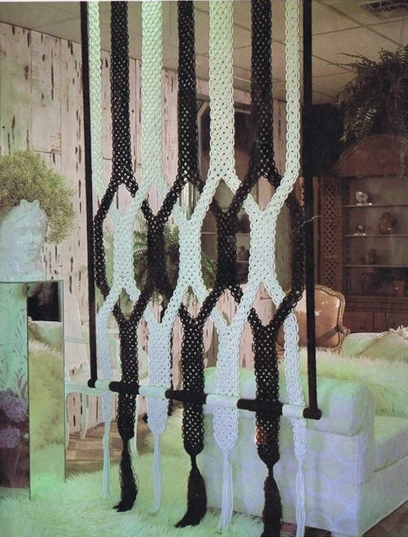 May include: A black and white macrame room divider with tassels hanging from the bottom. The divider is made of thick rope and is hung from a wooden dowel.