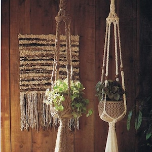 May include: Two macrame plant hangers with wooden beads, one in natural brown rope and one in white rope, hanging from a wooden wall. Both hangers have a tassel at the bottom and are holding potted plants.