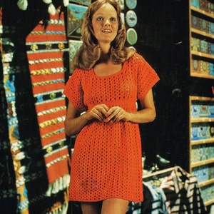 May include: A woman wearing a bright orange crochet mini dress with short sleeves. The dress has a loose fit and a crocheted pattern.
