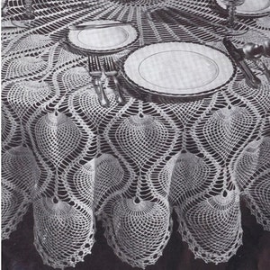 K&ouml;nnte beinhalten: Eine wei&szlig;e H&auml;keltischdecke mit einem gewellten Rand und einem Ananas-Muster. Die Tischdecke liegt auf einem Tisch mit zwei Tellern und Besteck.