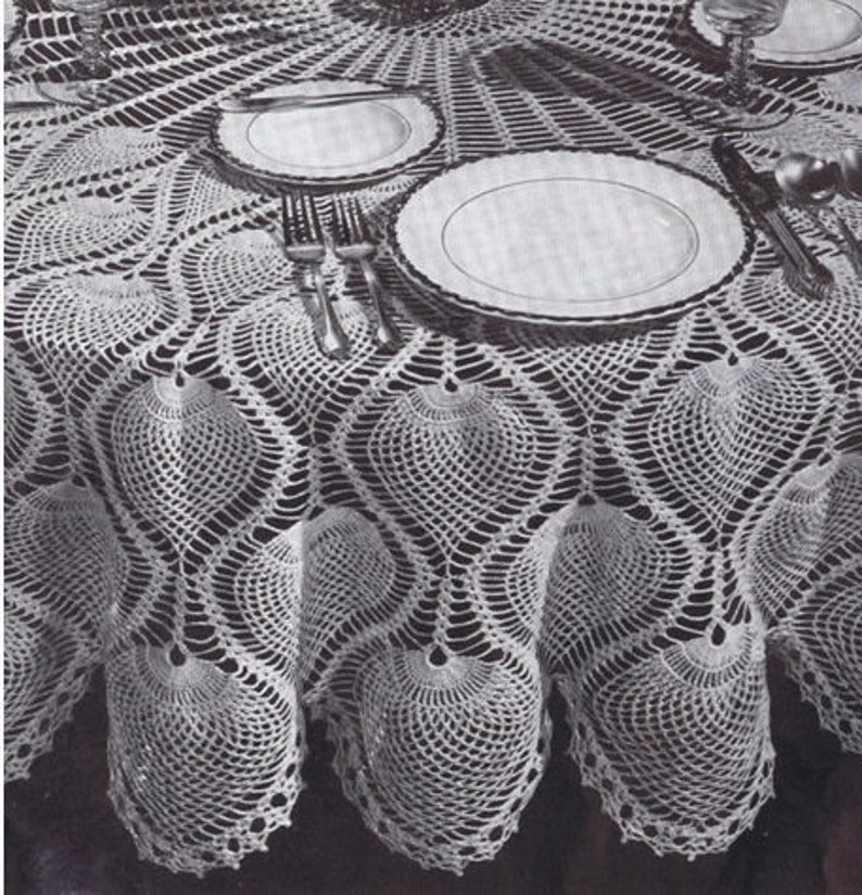 K&ouml;nnte beinhalten: Eine wei&szlig;e H&auml;keltischdecke mit einem gewellten Rand und einem Ananas-Muster. Die Tischdecke liegt auf einem Tisch mit zwei Tellern und Besteck.