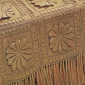 May include: A crocheted tablecloth with a brown and beige color scheme. The tablecloth features a repeating pattern of large, crocheted flowers. The tablecloth has a fringe border.